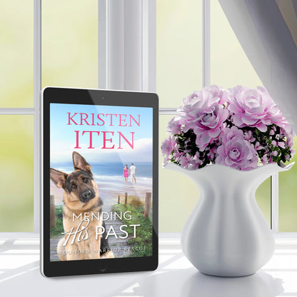 mending his past cover on ereader, sitting on table next to a vase of flowers.